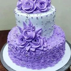 a three tiered cake with purple frosting roses on the top and bottom layer