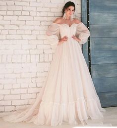 a woman in a white dress standing next to a brick wall with her hands on her hips