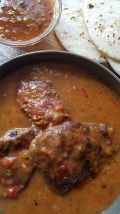 some food is in a bowl on a table with tortillas and pita bread