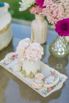 a white cake with pink flowers and a unicorn horn on it sitting on a plate