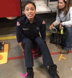 a woman in uniform sitting on a chair next to a fire truck and another woman standing behind her