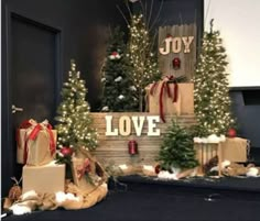 christmas trees and presents in front of a sign that says joy love with lights on them