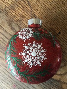 a red ornament with white flowers and green leaves on it sitting on a wooden table