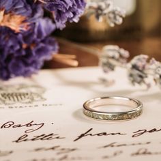 two wedding rings sitting on top of a piece of paper next to some purple flowers