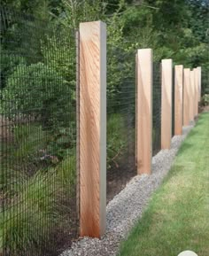 a row of wooden posts on the side of a fenced in area next to grass and trees