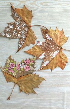 three leaves with flowers painted on them sitting on top of a wooden table next to each other