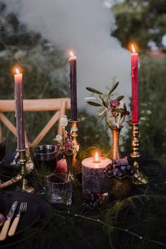 a table topped with candles and plates filled with food on top of a lush green field