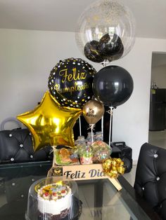 a table topped with black and gold balloons, cake and other party items on top of it