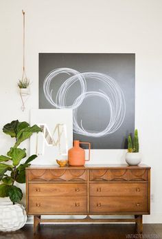 a dresser with two vases and a painting on the wall above it in a living room