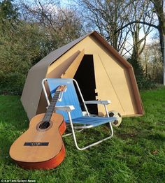 a guitar and chair in the grass next to a tent with an awning on it