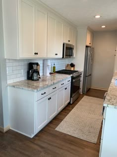 a kitchen with white cabinets and marble counter tops