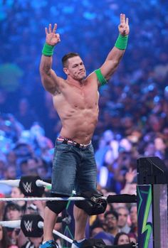 a man standing on top of a wrestling ring holding his hands up in the air