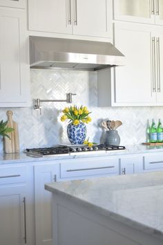 a kitchen with white cabinets and marble counter tops, yellow flowers in a blue vase on the stove