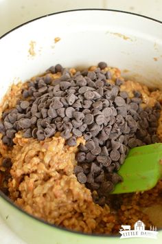 chocolate chips and oatmeal are mixed together in a bowl with a green spoon