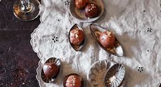 four chocolate covered desserts are on small plates with silver spoons next to them