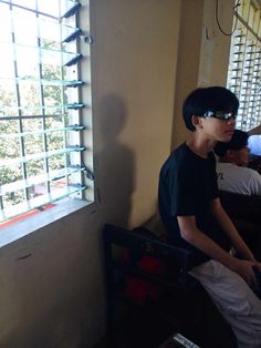 a young man sitting on top of a chair next to a window with blind shades