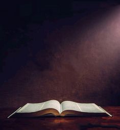 an open book sitting on top of a wooden table next to a light that is turned on