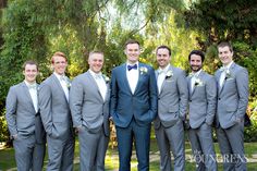 a group of men standing next to each other wearing suits and bow ties in front of trees