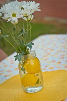 a vase filled with lemons and daisies on top of a yellow table cloth