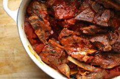 a pot filled with meat and sauce on top of a wooden table