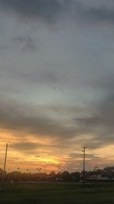 the sun is setting over a field with trees and buildings in the backround