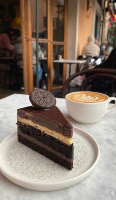 a piece of cake on a plate with a cup of cappuccino in the background