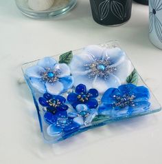 a glass plate with blue flowers on it sitting on a table next to other vases