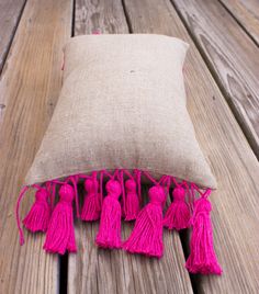 a pillow with pink tassels is on a wooden bench