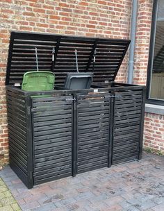 an outdoor storage unit with two bins and a trash can in front of a brick building