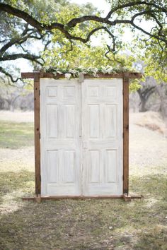 an open white door sitting on top of a grass covered field next to a tree