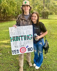 a young man and woman standing next to each other holding a sign that says it's home coming season & i'm hunting for a date you game yes no