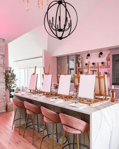 a dining room with pink chairs and paintings on the wall in front of an island