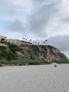 the beach is empty and there are palm trees on the hill behind it in the distance