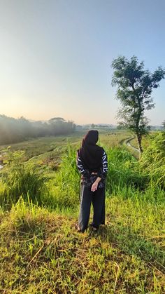 a person standing in the grass with a hood over their head looking down at something