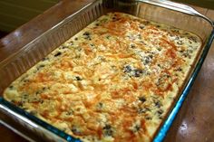 a casserole dish with cheese and black olives in it on a wooden table