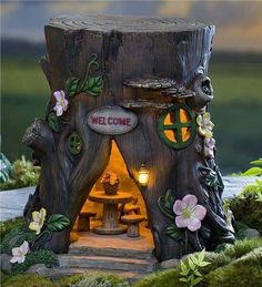 a small wooden tree stump with a welcome sign on it's side and flowers around the entrance