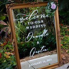 a mirror that is sitting on the ground in front of some plants and flowers, with a sign reading welcome to our wedding bride and groom