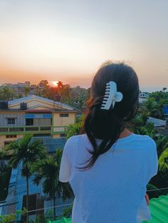 a woman standing on top of a roof with a hair comb in her hand and the sun setting behind her