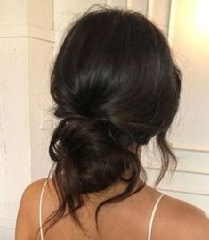 the back of a woman's head with her hair in a low bun, wearing a white tank top