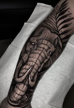 an elephant tattoo on the arm with leaves and feathers in black and grey colors is shown