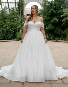 a woman in a white wedding dress standing on a brick walkway with greenery behind her