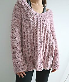 a woman is standing in front of a white wall wearing a pink crochet sweater