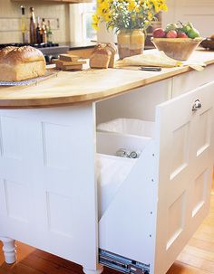 an open cabinet in the middle of a kitchen counter with bread and fruit on it