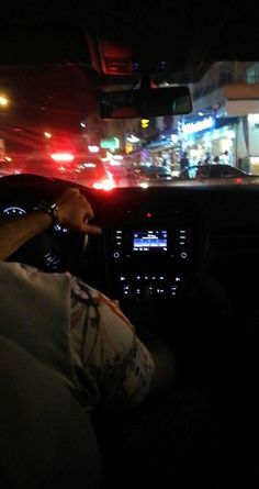 a person sitting in the driver's seat of a car at night with city lights behind them