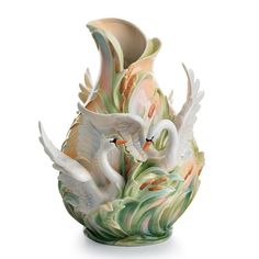 two white swans in a vase with green leaves on the bottom and one is holding its wings