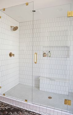 a white tiled bathroom with gold trim and glass shower doors, along with a rug on the floor