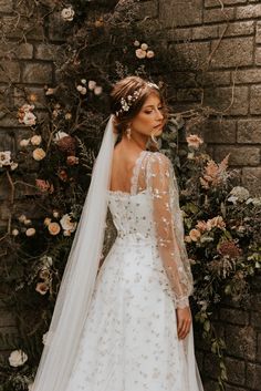 a woman in a wedding dress standing next to a brick wall with flowers on it