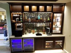 a home bar with liquor bottles and glasses on the shelves, along with two mini fridges