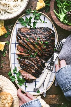 a person holding a knife and fork over a steak on a plate with other food