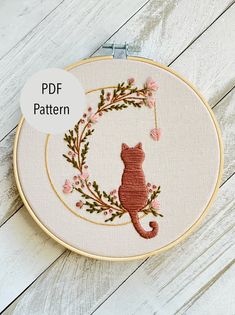 an embroidery pattern with a cat in the center and flowers around it on a white wooden background